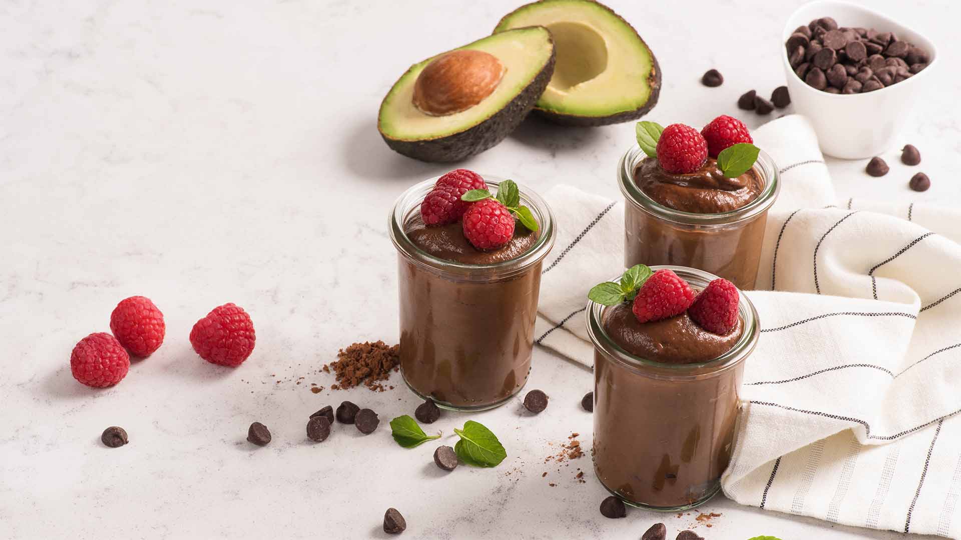 Chocolate Avocado Mousse in glass cups with avocados in the background